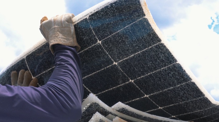 Técnico de luva segura um módulo fotovoltaico danificado e flexionado contra o céu
